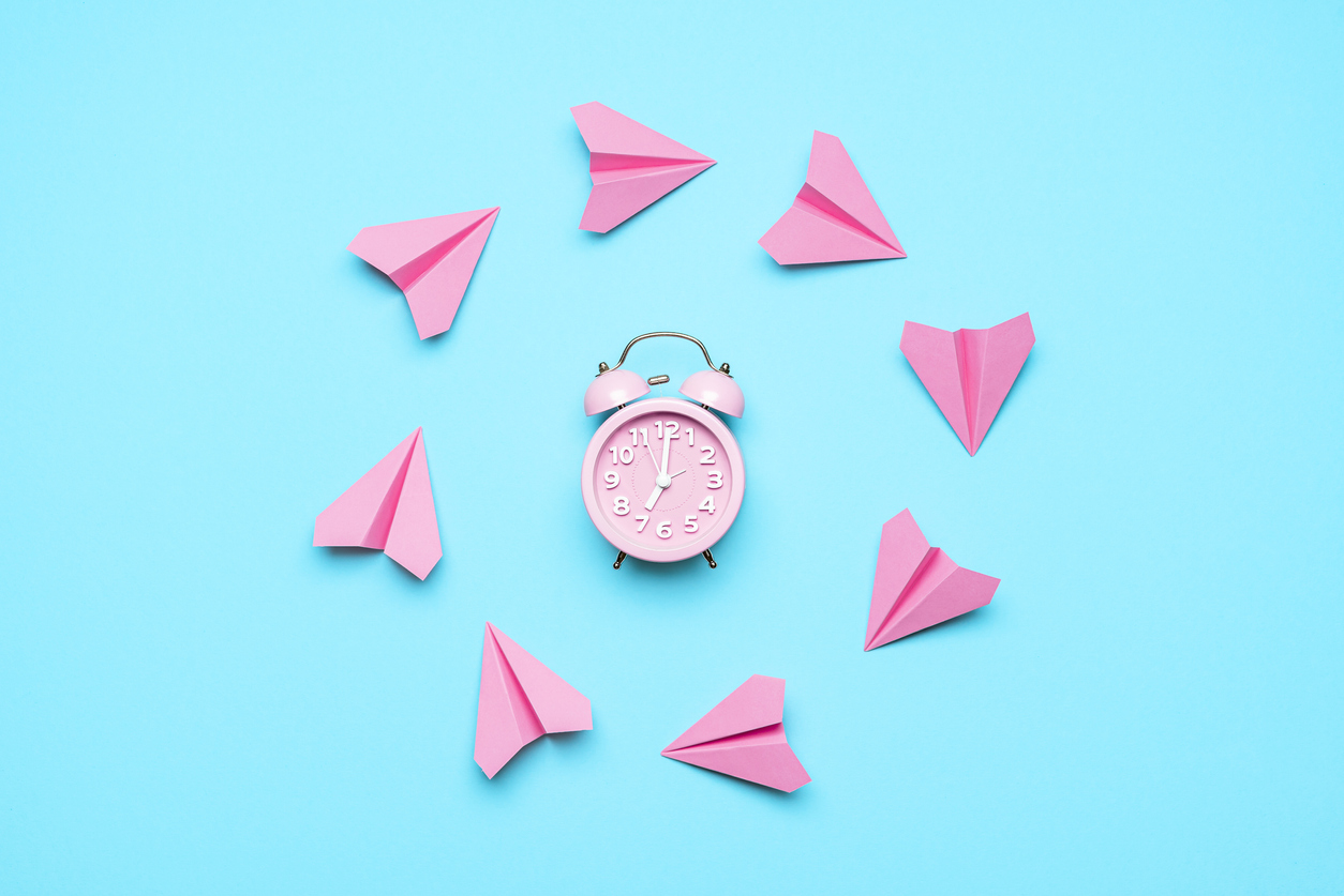 a blue background with a pink alarm clock. around the clock are pink paper airplanes forming a circle.